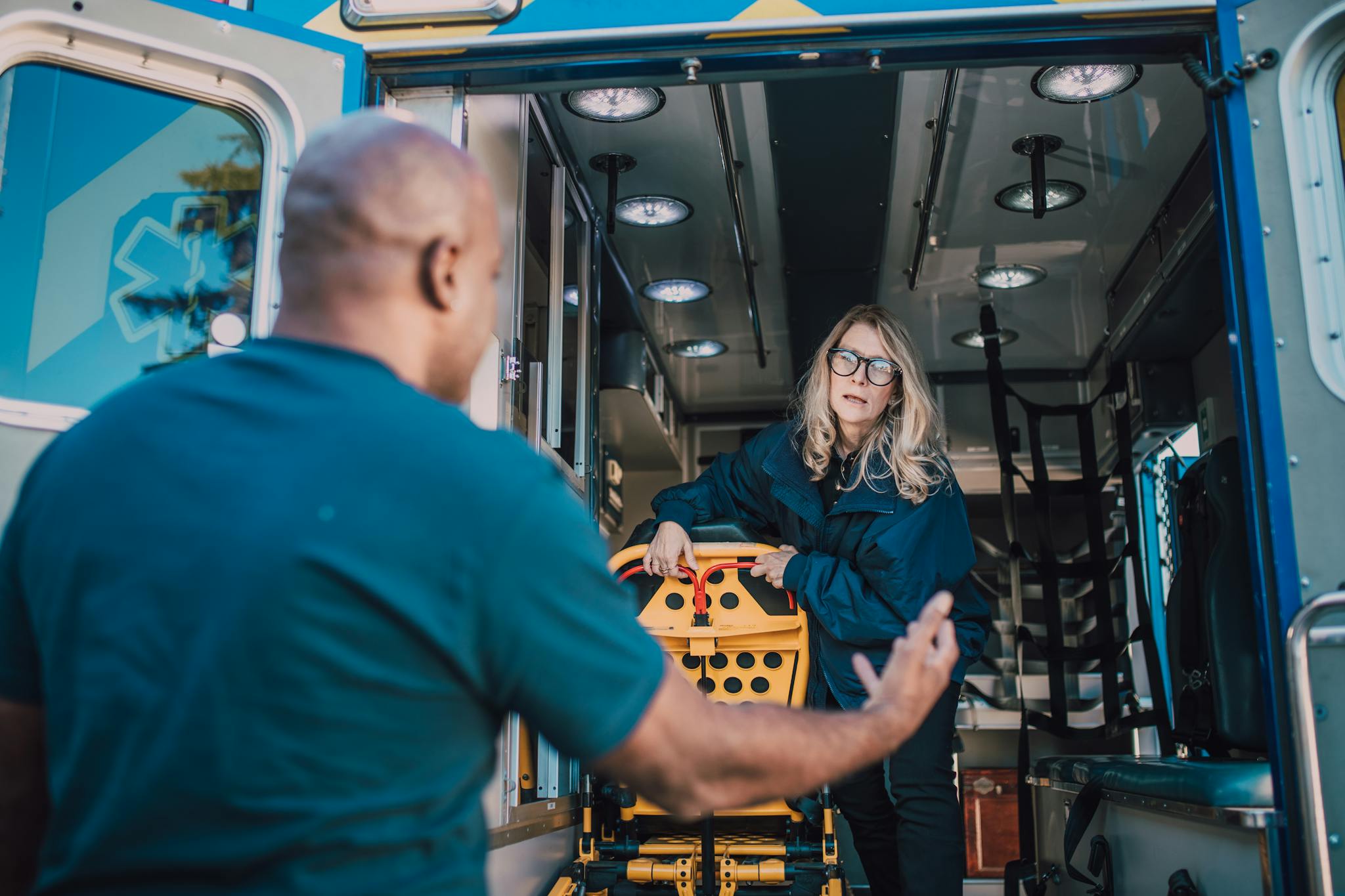 Paramedics working inside an ambulance, preparing a stretcher for an emergency response.