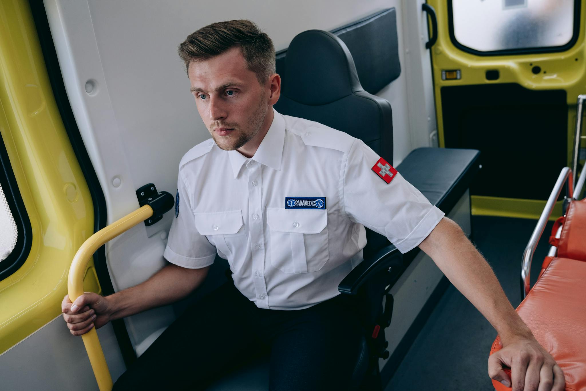 Focused paramedic in uniform sitting inside an ambulance, ready for action.