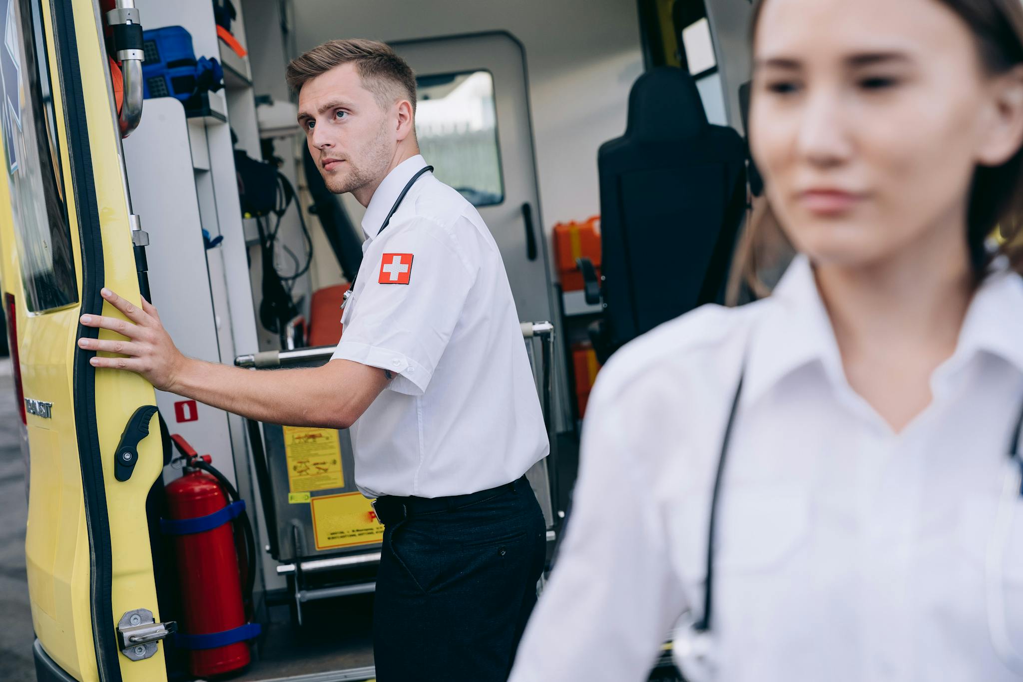 Two paramedics in uniform prepare an ambulance for emergency response, emphasizing teamwork and readiness.